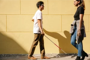 Незрящ човек с бастун върви срещу млада жена на улицата